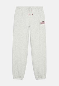 Hellgraue Jogginghose aus weichem Material, mit elastischem Bund und Kordelzug, sowie rotem Logo-Text auf dem linken Oberschenkel.