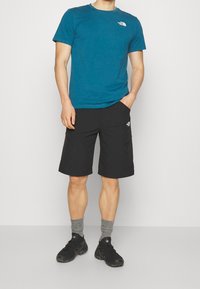 Blå crew-neck t-shirt tillsammans med svarta cargoshorts. Texturerat tyg med logotypdetalj. Grå ankelsockor och svarta vandringsskor kompletterar outfiten.