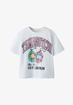 Camiseta blanca de manga corta con texto rosa "Tamagotchi", ilustraciones de juguetes Tamagotchi azules y rosas, y "EST. JAPAN" en texto negro debajo.