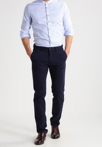 Camicia button-down azzurra con righe bianche, abbinata a pantaloni blu navy. Scarpe marroni completano l'outfit. Design semplice e su misura.