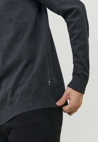Dunkelgrauer gestrickter Pullover mit einem gerippten Saum und Bündchen. Hat ein kleines Logo nahe dem Saum. Weiche Textur und lässige Passform.