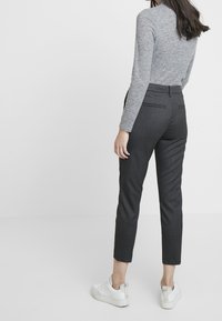 Grijze langslavige top en donkere gestreepte broek met taps toelopende benen, gecombineerd met witte sneakers. Heeft achterzakken en een aansluitend ontwerp.