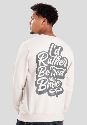 Sudadera gris clara con cuello redondo, con un gran texto negro en la parte posterior: "Preferiría estar cansado que en quiebra." Textura suave.