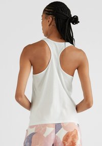 Jasnoszary top na ramiączkach z designem racerback. Gładki materiał o luźnym kroju. W połączeniu z spodniami w pastelowe wzory.