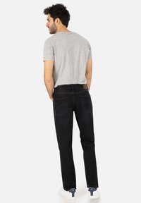 Herren graues T-Shirt, kombiniert mit schwarzen Jeans; verfügt über Taschen und ein braunes Leder-Patch. Abgerundet mit weißen Sneakers.
