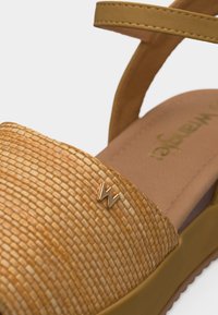 Ταμπά πλεκτό σανδάλι με χρυσό έμβλημα "W" στο μπροστινό λουράκι και ρυθμιζόμενο λουράκι αστραγάλου σε επίπεδη σόλα.