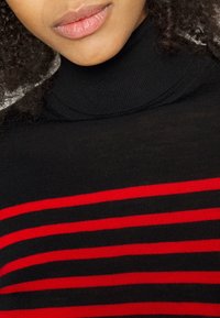 Maglione a collo alto nero con strisce orizzontali rosse. Tessuto a maglia, design aderente e dettaglio del colletto a costine.