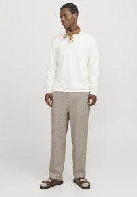 Camisa blanca de manga larga, pantalones beige a rayas, bufanda marrón y sandalias de tiras marrones. Diseño minimalista con un corte relajado y tejido texturizado.