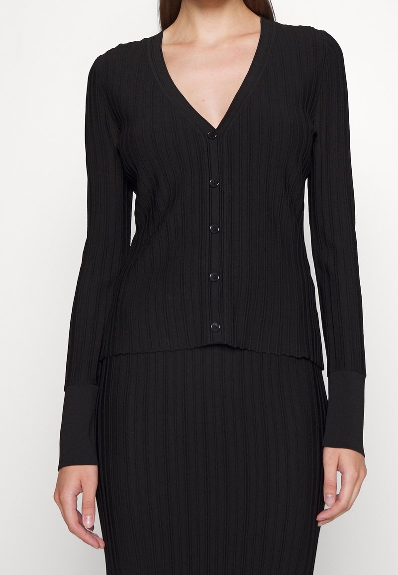 Black ribbed cardigan with a v-neckline, long sleeves, and five front buttons. Features textured fabric with a scalloped hem.