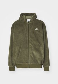 Olivgrön kordflöjel zip-up hoodie med snörning i huvan, framfickor och en vit Adidas-logo på bröstet. Mjuk textur och ribbade ärmslut.