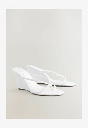 Para białych sandałów na koturnie z cienkimi krzyżującymi się paskami i odkrytymi palcami, prezentowanych na neutralnym tle.