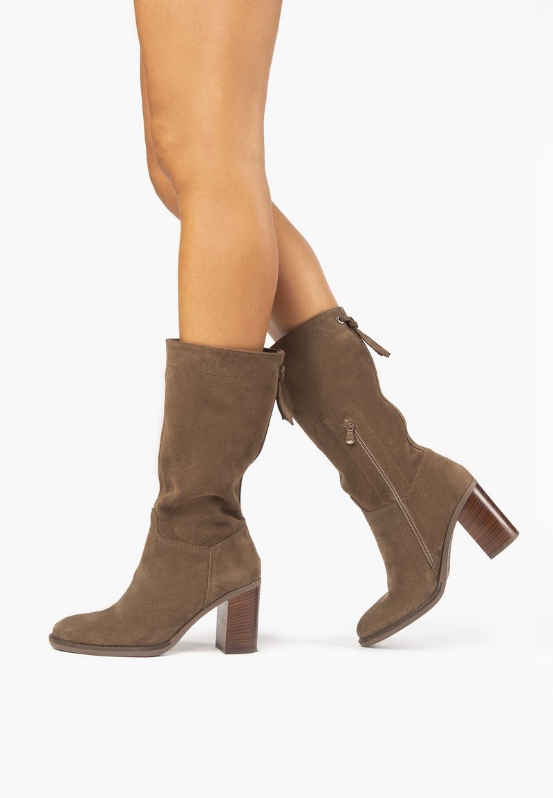 Bottes montantes en daim marron avec un talon bloc, dotées d'une fermeture éclair latérale et d'un nœud décoratif à l'arrière. Texture lisse, silhouette simple.