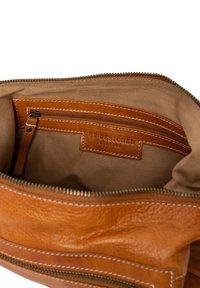 Interno di una borsa in pelle marrone con fodera in tessuto beige, dotata di una tasca e un'etichetta. Le cuciture visibili aggiungono dettagli. Chiusura con zip.