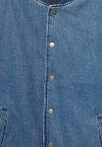 Jachetă din denim cu o țesătură de culoare bleu deschis, cu nasturi tip snap și buzunare laterale. Materialul are un finisaj texturat cu cusături vizibile.