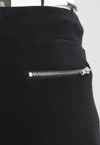 Svarta sweatpants med en slät textur, med en sidoficka med dragkedja och silverdetaljer. Lättsam design som passar för vardagsbruk.