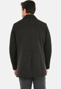 Giacca esterna nera con colletto strutturato, texture liscia, lunghezza media e vestibilità sagomata. Design minimalista senza motivi visibili.