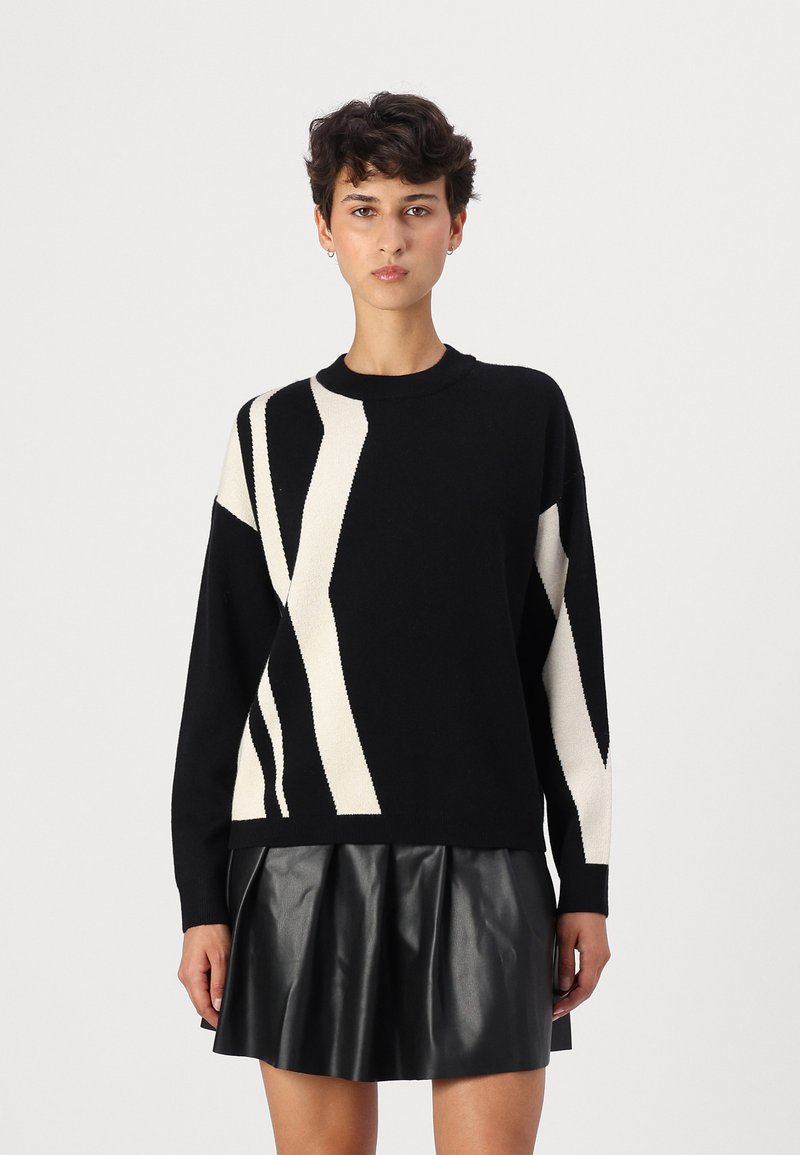 Black sweater with white abstract stripes, knit material, round neckline, relaxed fit, paired with a black pleated leather skirt.