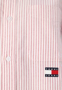 Červená a biela pruhovaná košeľa na gombíky s náprsníkovou vreckom a nášivkou "TOMMY JEANS" s čierno-bielymi akcentmi.