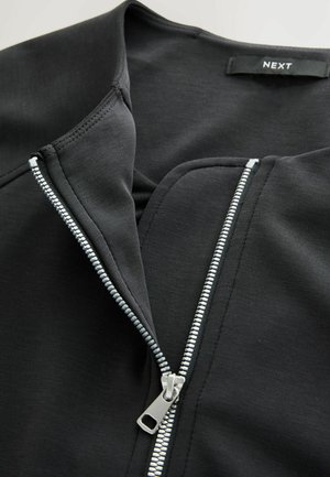 Schwarze Jacke mit Reißverschluss, die eine glatte Textur, flache Nähte und einen silbernen Reißverschluss mit einem Anhänger, der mit 'NEXT' beschriftet ist, am Kragen aufweist.