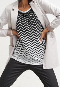 Ljusrosa kavaj över en topp med svart-vitt zigzag-mönster. Outfiten matchas med svarta byxor. Släta texturer och modern design.