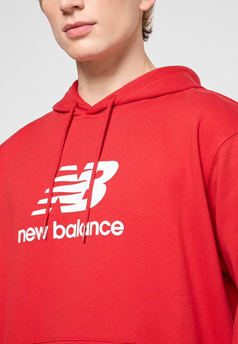 Hoodie en coton rouge avec un grand logo blanc New Balance sur la poitrine, capuche avec cordon de serrage et texture douce et lisse.