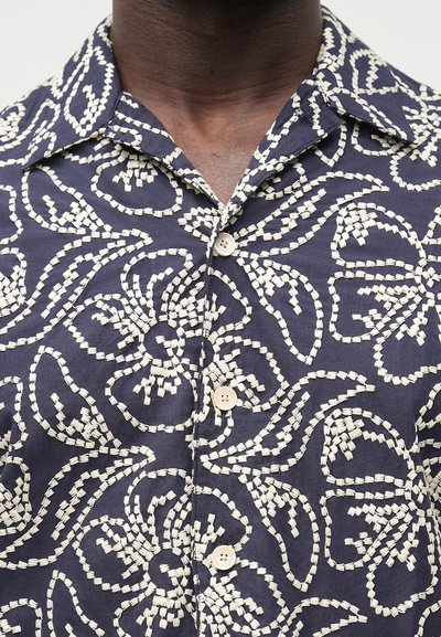 Tmavomodrá košeľa s bielym kvetinovým a vlnkovým vzorom, krátkymi rukávmi a golierom. Na prednej strane sú dvoma svetlými gombíkmi.