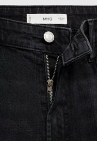Jeans en denim noir avec un bouton en métal et une braguette à glissière. Taille plate, couture standard, et une étiquette d'entretien visible à l'intérieur.