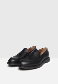 Mocassini in pelle nera con punta arrotondata, caratterizzati da dettagli di cucitura discreti e da una fascia decorativa sulla parte anteriore. Design con suola piatta.