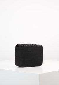 Borsa a mano nera in tessuto con bordo superiore texture in perline, forma rettangolare e finitura liscia, appoggiata su una superficie bianca.