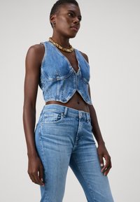 Denim crop top met een diepe V-hals, lichtblauwe kleur, en voornaden. Gecombineerd met lichtblauwe skinny jeans met gouden hardware accenten.