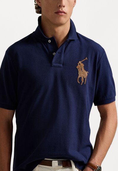 Navyblauwe poloshirt gemaakt van textuurstof, met een opvallend bruin geborduurd paardenlogo op de linkerborst en twee knopen bij de kraag.