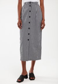 Schwarz-weiß karierte Midi-Rock mit vorderen Knöpfen, hoher Taille und Falten, aus Baumwollstoff; kombiniert mit offenen schwarzen Blockabsätzen.