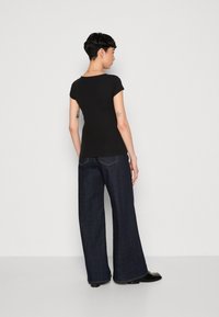 Haut noir à rayures et à manches courtes associé à un jean sombre à jambes larges, avec une couture distincte et une coupe décontractée. Texture lisse, design minimal.
