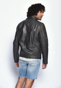 Schwarze Motorradlederjacke mit gesteppten Details an den Schultern und Seiten, taillierter Schnitt und glatte Textur. Falten auf dem Rücken.