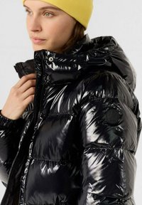 Giacca a puffo nera lucida con zip e chiusura a pressione, dotata di cappuccio, polsini elasticizzati e una patch con logo sulla manica.