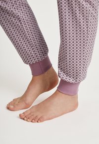 Paarse joggers met een geometrisch patroon en elastische boorden. Blote voeten zijn zichtbaar, wat de zachte textuur van de stof benadrukt.