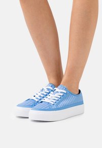 Sneakers in tela a righe blu con lacci bianchi e una spessa suola in gomma bianca, caratterizzati da strisce diagonali e un design a profilo basso.