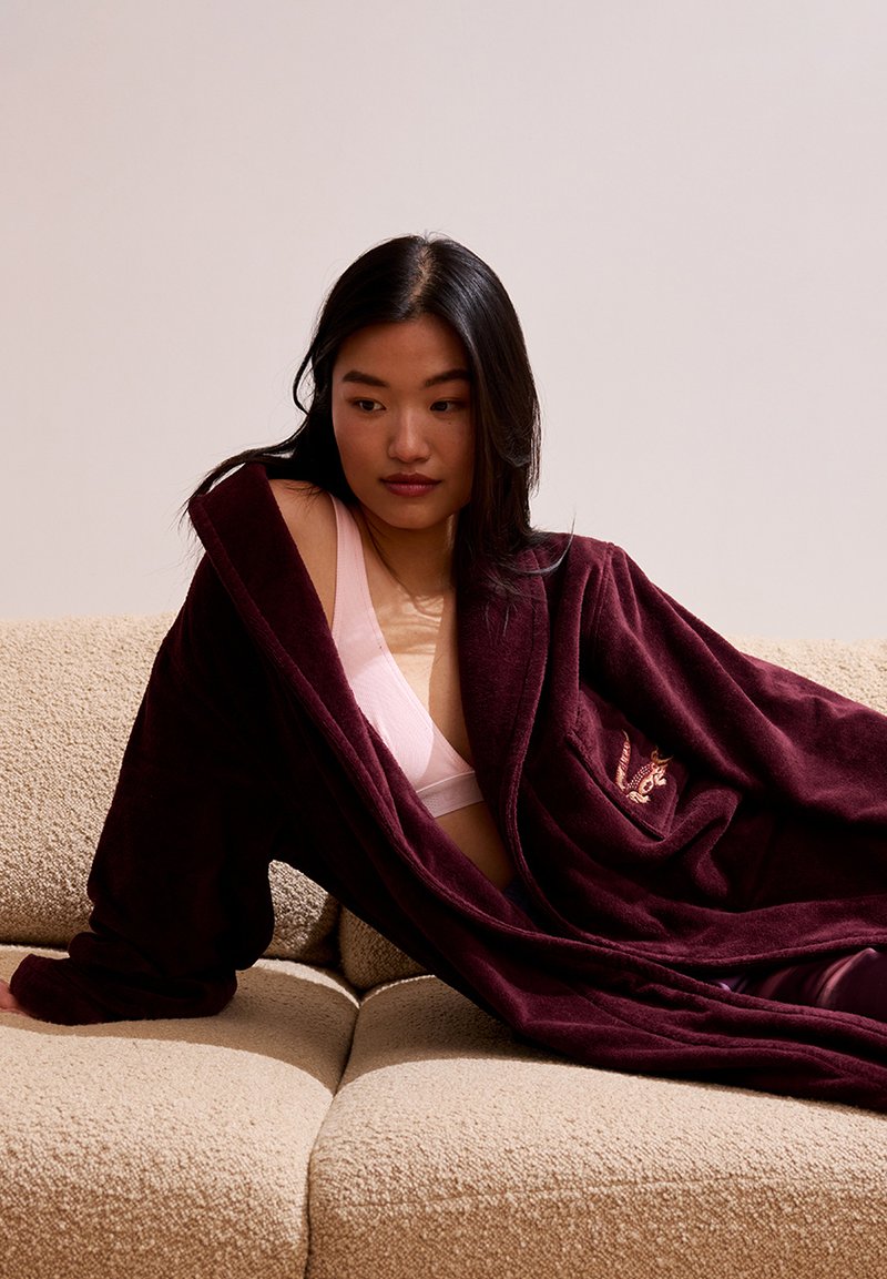 Burgundy fleece robe with open front and large pockets. Soft texture, mid-length sleeves, and embroidered accent on the chest.