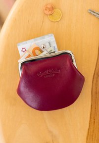 Burgundi nahast mündikott metallist sulguriga. Selles on eurod ja nähtav kaart. Kaks münti on selle kõrval puidust pinnal.