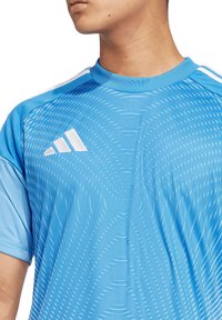 Hellblaues Sportshirt mit Rundhals, das ein strukturiertes Muster und ein weißes Adidas-Logo auf der Vorderseite aufweist. Kurze Ärmel.