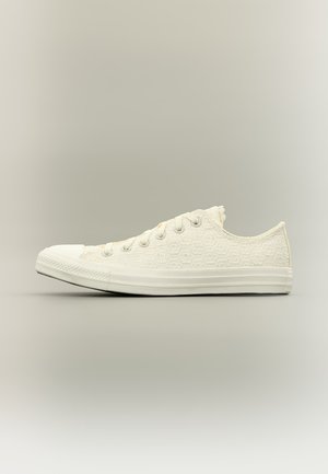 Sneakers blanches basses avec dessus en tissu texturé et semelle blanche en caoutchouc, montrées de profil sur fond neutre.