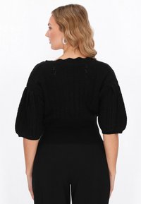 Schwarzer gestrickter Pullover mit strukturierten Mustern; hat weite, puffige Ärmel und einen taillierten Rippabschluss. Die Rückansicht zeigt dezente Details am Kragen.