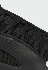 Czarny but sportowy z teksturowanego materiału siatkowego, płaskimi sznurówkami oraz gładką gumową podeszwą o zaokrąglonych krawędziach i wzmocnionymi detalami.