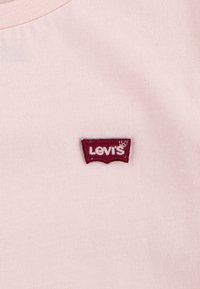 Camiseta de algodón rosa claro con un logo de Levi's bordado en rojo sobre un parche clásico de mangas batwing, cuello redondo y textura suave.