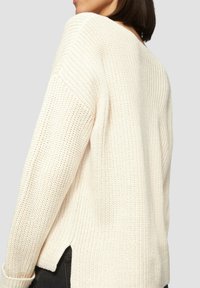Cremefarbener Strickpullover mit lockerer Passform, breiter Rippstruktur und seitlichen Schlitzöffnungen zur Belüftung, mit einem V-Ausschnitt.