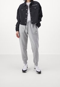 Czarna krótka kurtka z zatrzaskami i logo "Nike Air", połączona z szarymi spodniami dresowymi. Białe sneakersy z czarnymi akcentami dopełniają stylizację.