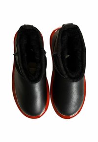 Schwarze Lederstiefel mit einem weichen schwarzen Fellfutter und roten, glänzenden Gummisohlen. Das Design weist einen niedrigen Knöchelanschnitt und eine abgerundete Zehenform auf.