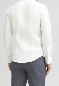 Witte lange mouwen shirt met een soepele textuur, ronde zoom en met knopen afgewerkte manchetten, gecombineerd met grijs gestreepte broek.