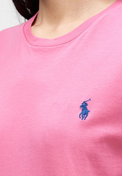 Rózsaszín pamut póló bordázott, kerek nyakrésszel és egy kis kék hímzett ló és lovas logóval a bal mellrészen.