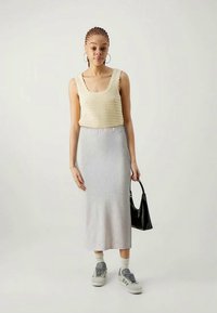 Camisola de malha creme com bordas em scallop, combinada com uma saia midi cinza de malha canelada. O modelo usa sapatilhas cinzas e segura uma carteira preta.